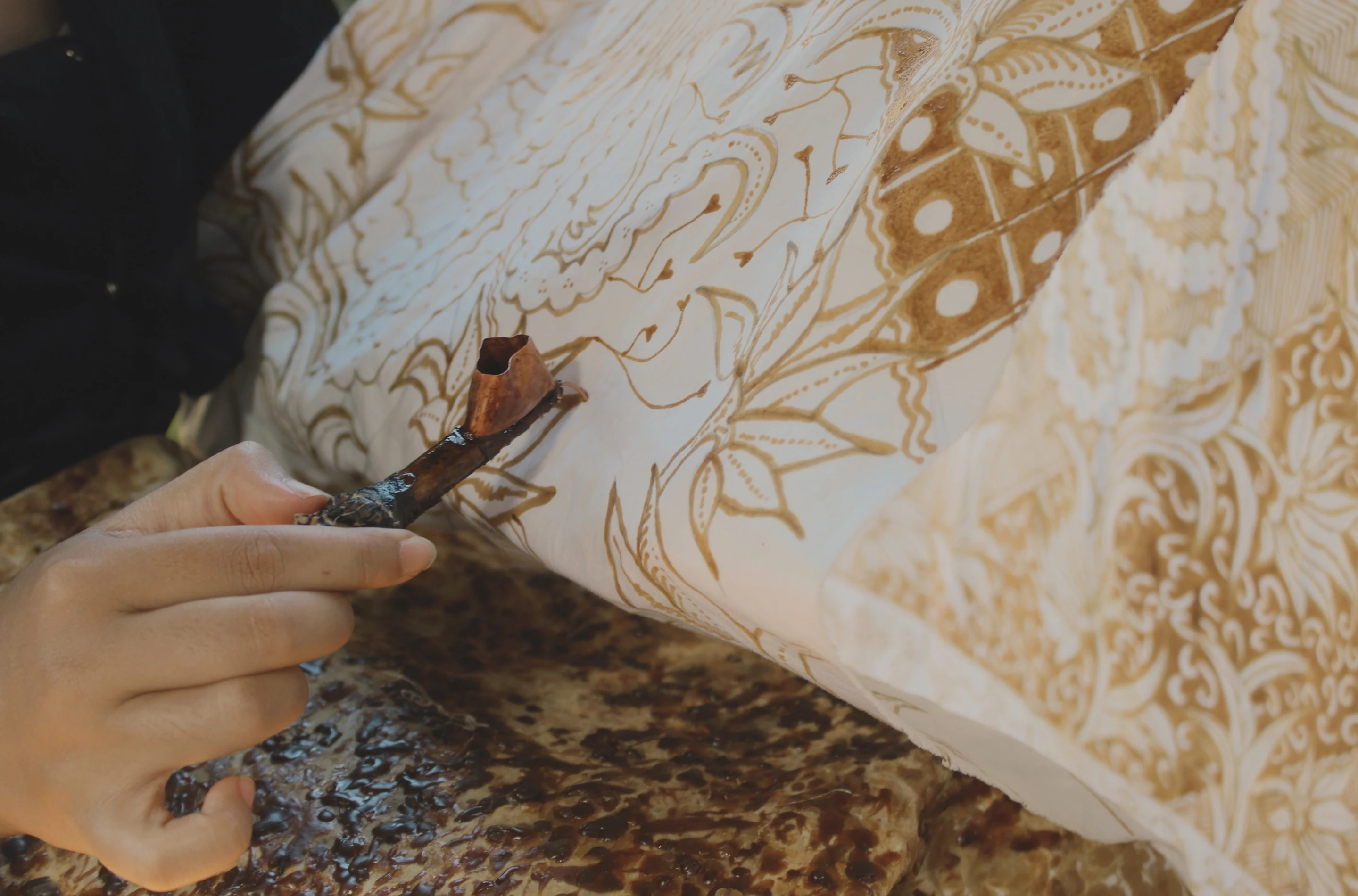 Artisan hand-drawing wax onto batik cloth with a canting